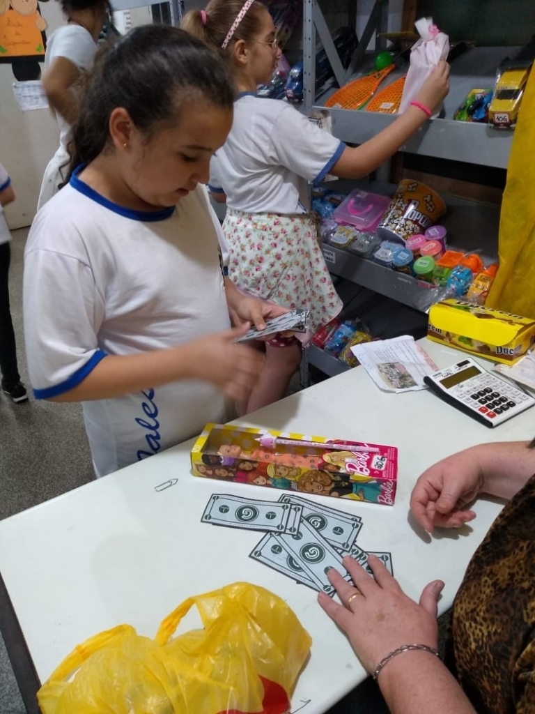 As crianças aprendendo e brincando ao trocarem o dinheiro escolar por produtos